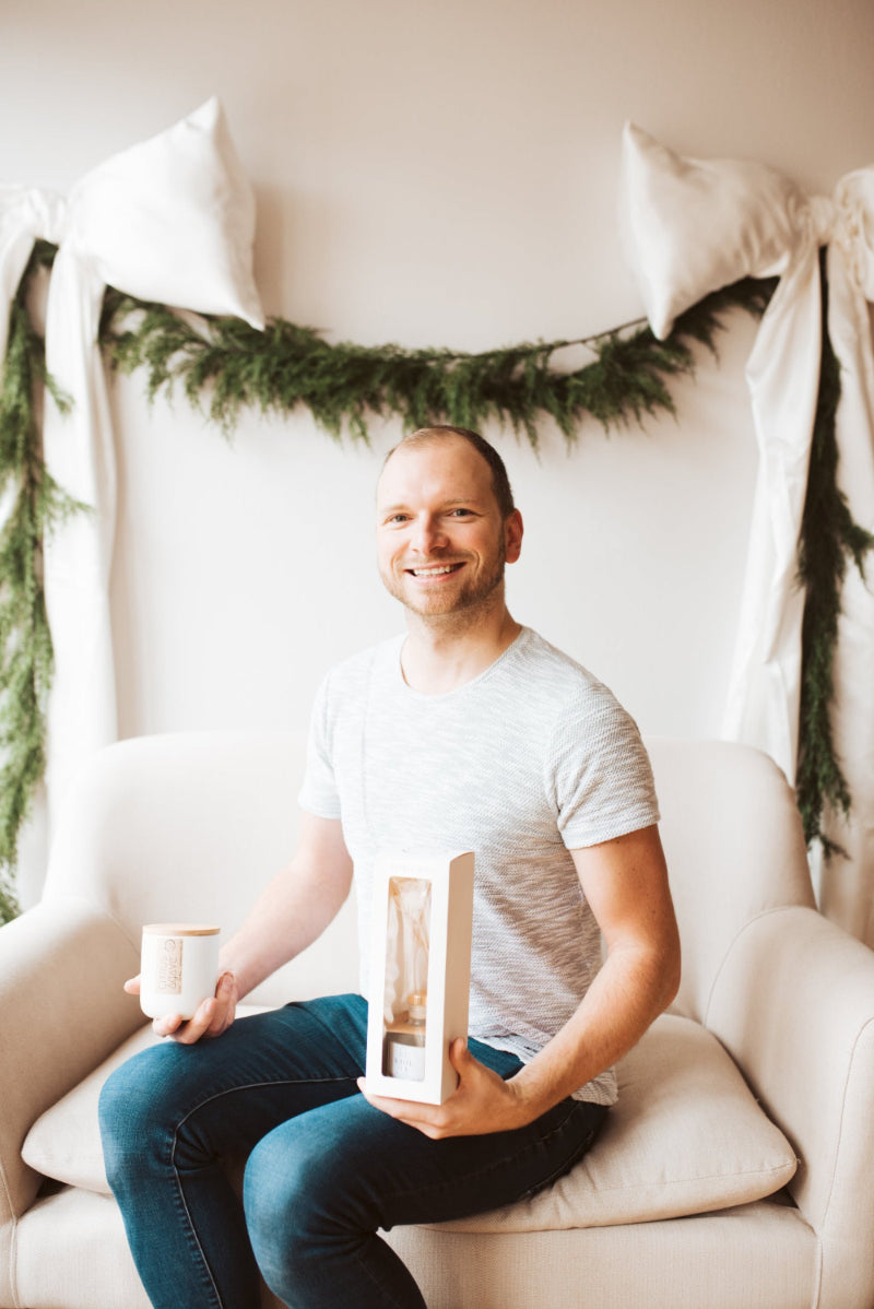 Man sitting on a couch holding a gift box with Christmas decorations in the background