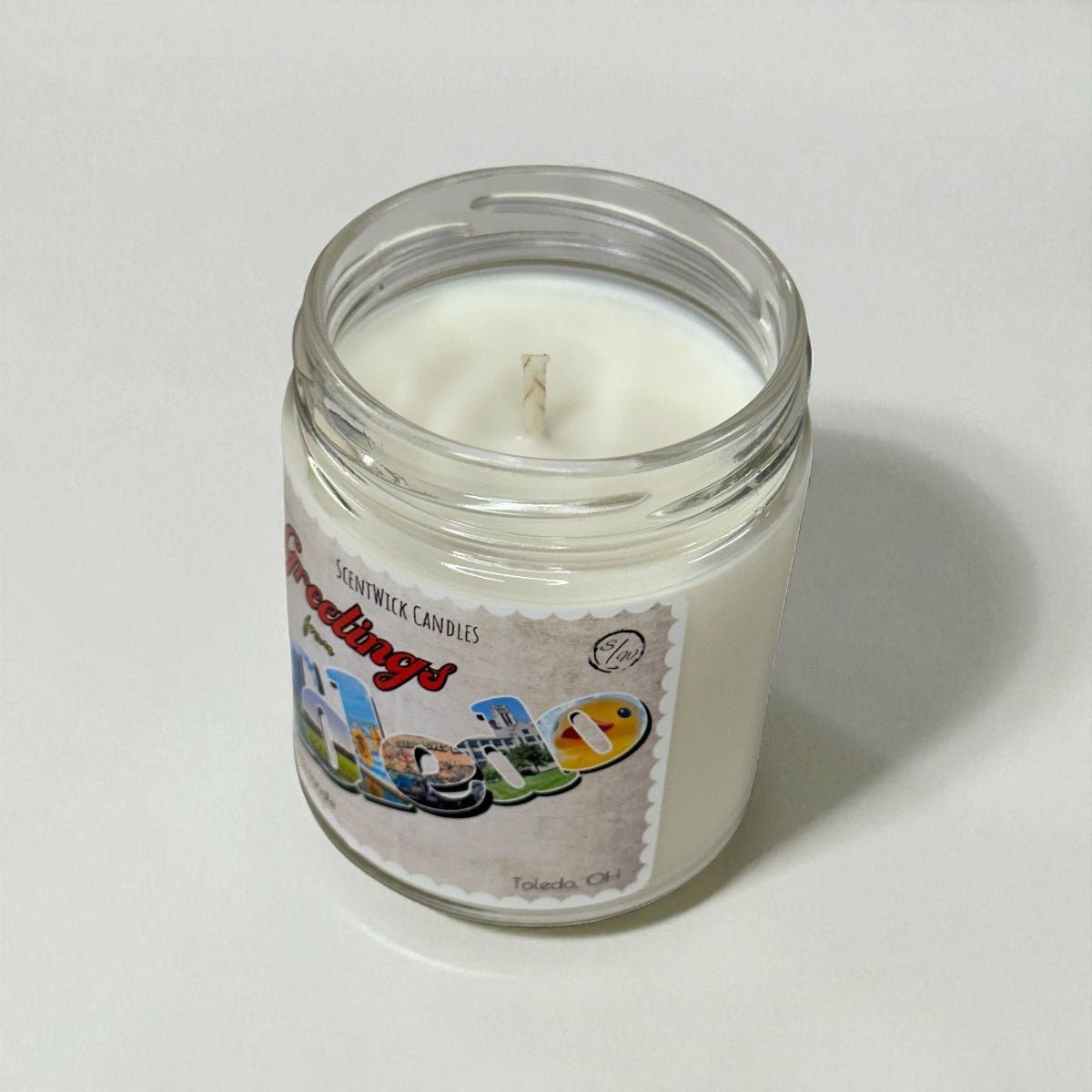 Candle in a glass jar with a colorful Toledo label on a white background
