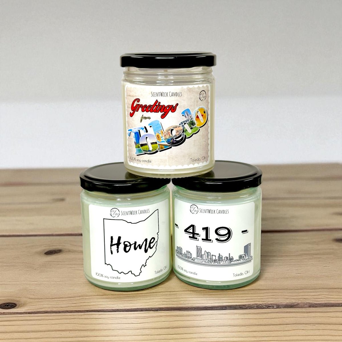 Three Toledo soy candles with black lids on a wooden surface