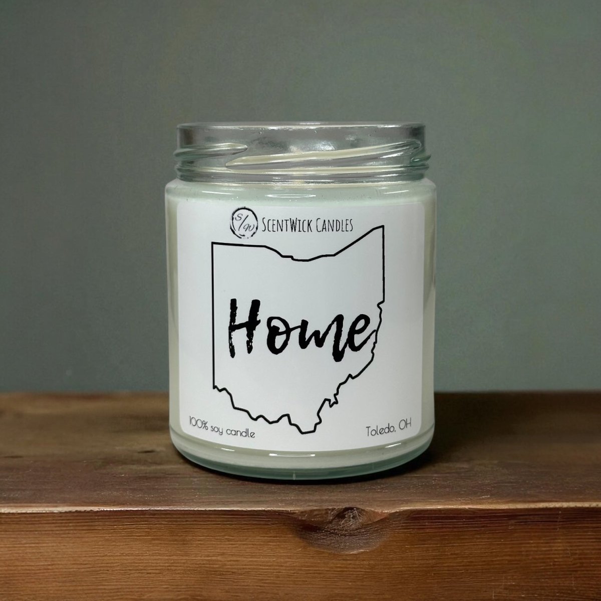 Candle in a glass jar with a 'Home' label on a wooden surface and gray background