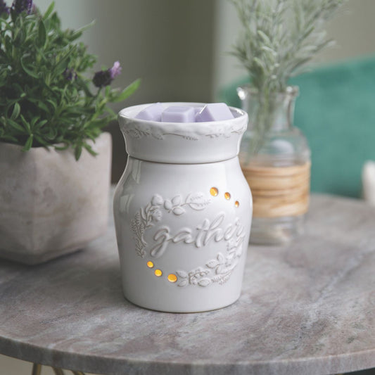 White ceramic wax warmer with 'gather' text on a marble surface with plants in the background