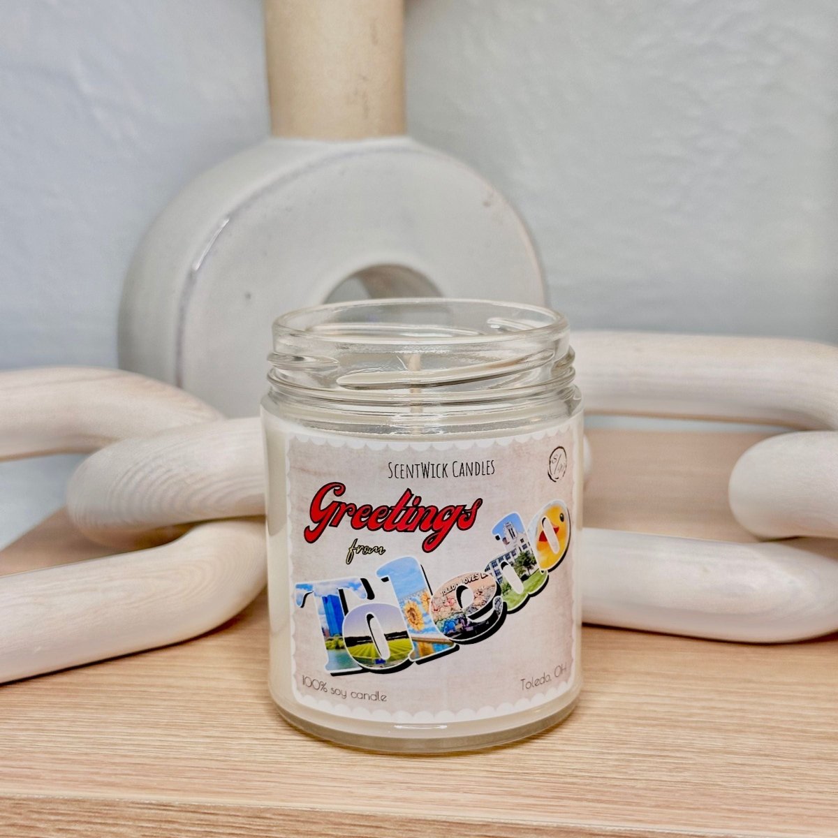 Scented candle jar with 'Greetings' label on a wooden surface