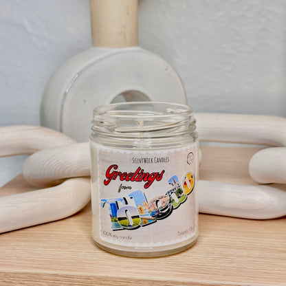 Scented candle jar with 'Greetings' label on a wooden surface