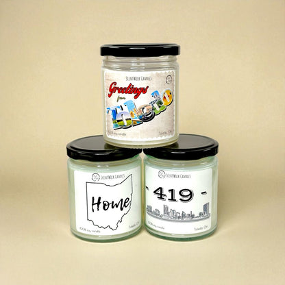 Three Toledo, Ohio, candles with black lids on a beige background