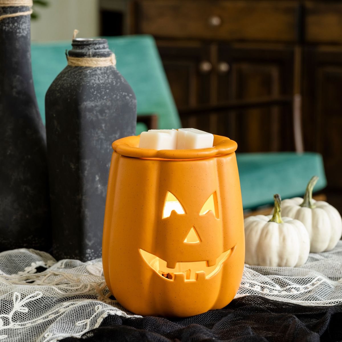 Orange jack-o'-lantern-shaped wax warmer on a table with decorative items.