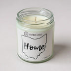 Candle in a glass jar with a 'Home' label on a white background