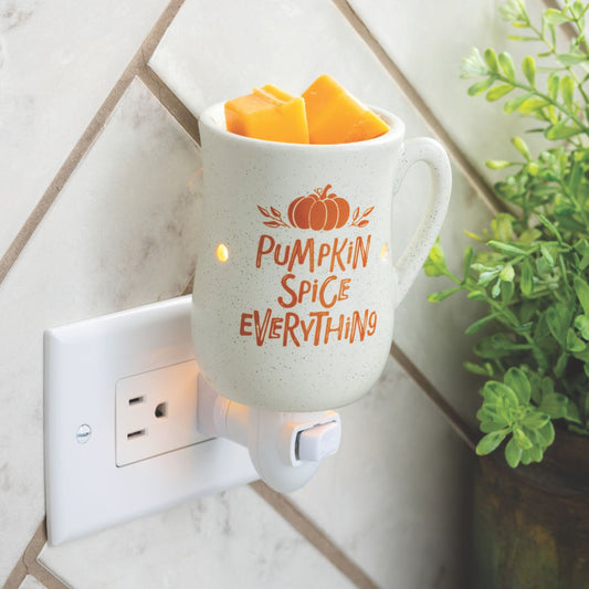 White fall wax warmer 'Pumpkin Spice Everything' text, plugged into a wall socket with a plant in the background.